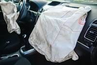 Innenansicht eines Autos mit einem ausgelösten Airbag auf dem Armaturenbrett und einem weißen Tuch auf dem Fahrersitz.