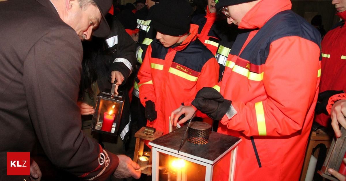 Mehrere Personen in Sicherheitsausrüstung sind um eine Laterne versammelt und zünden Kerzen an. Eine Person mit schwarzem Hut hält eine brennende Kerze, während andere ähnliche Aktivitäten durchführen.