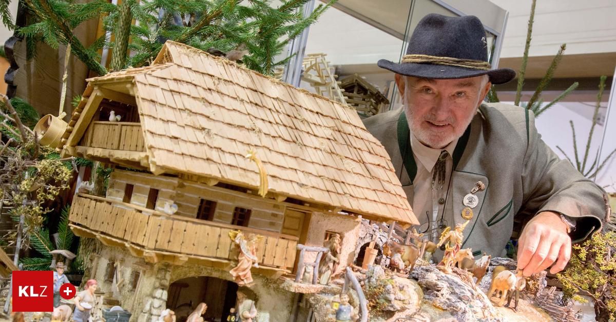 Ein älterer Mann mit Hut steht neben einer detaillierten Holzminiatur eines Dorfhauses mit Figuren und Tieren.