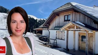 Eine Frau steht vor einem verschneiten Gebäude mit dem Schild Jaucha Haus. Dahinter ist eine Bergkette zu sehen.