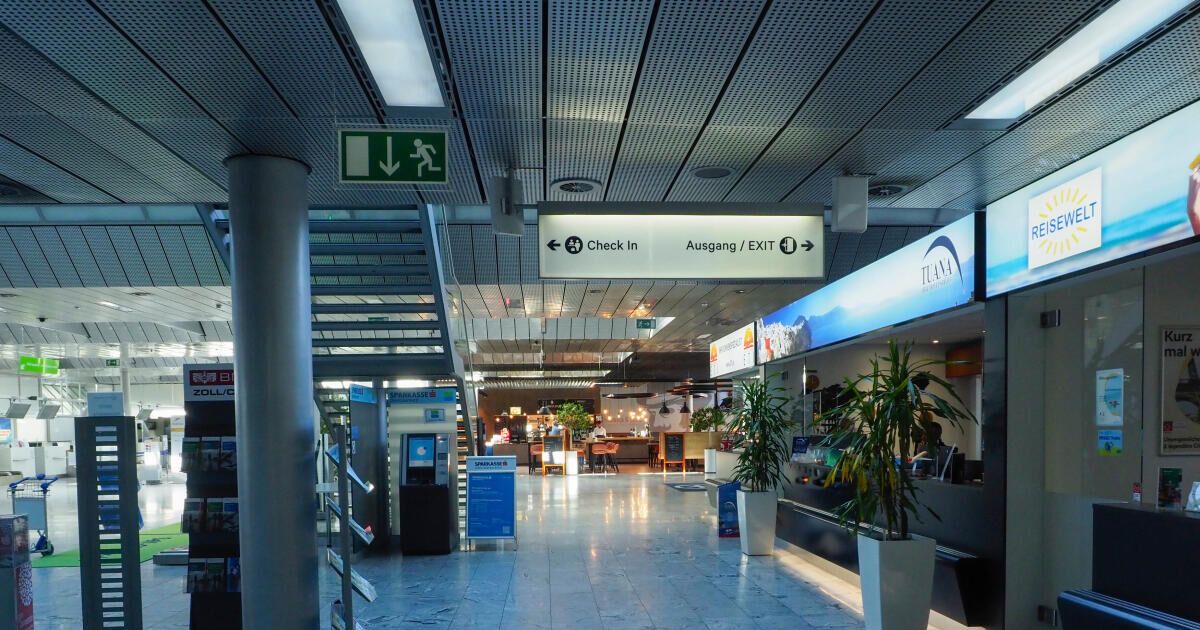 Ein Flughafenterminal mit einem Schild für Check-In und Ausgang/Ausgang. Der Boden ist glänzend und es gibt Topfpflanzen auf beiden Seiten.