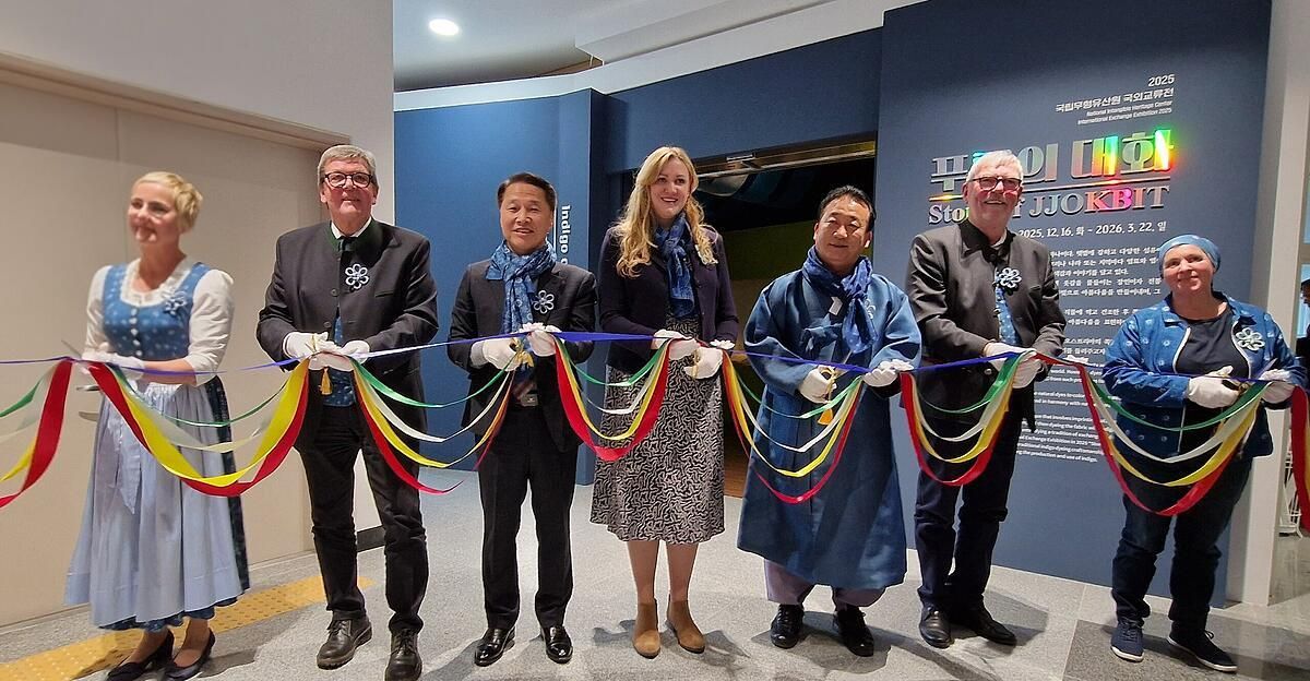 Fünf Personen, drei Männer und zwei Frauen, in formeller Kleidung, schneiden ein Band mit bunten Bändern. Hinter ihnen befindet sich eine blaue Wand mit fremdsprachigem Text.