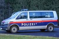Ein weiß-blauer Polizeitransporter mit dem Wort Polizei an der Seite fährt auf einer Straße mit Gras am Straßenrand.