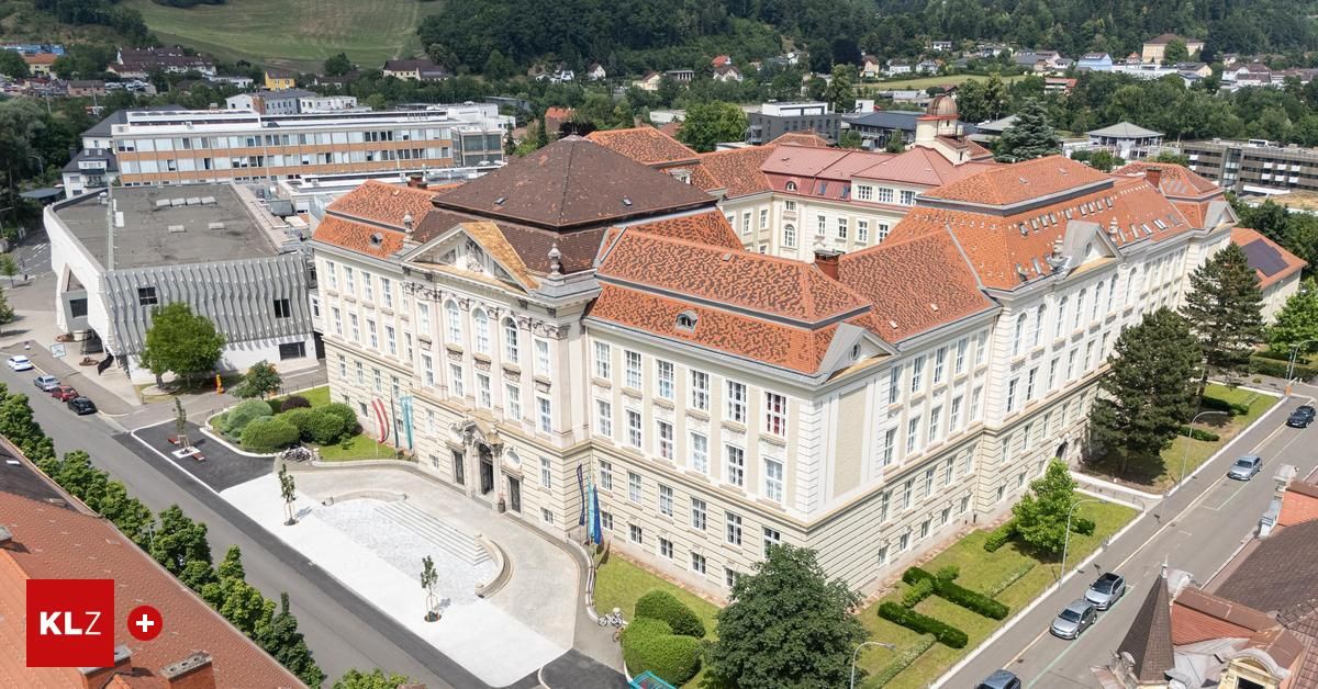 Ein Luftbild eines großen, klassizistischen Gebäudes mit mehreren Flügeln, roten Dächern und vielen Fenstern, umgeben von einem Garten und modernen Gebäuden.