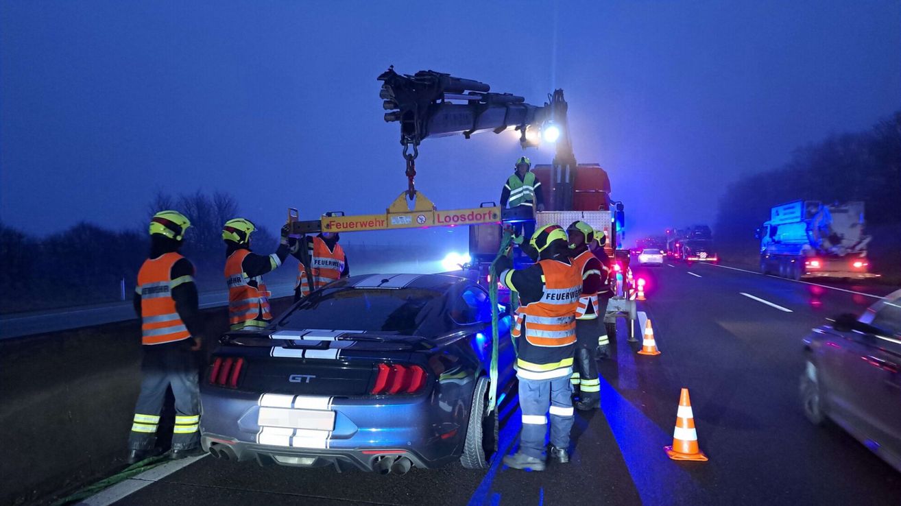 Ein beschädigter Ford Mustang GT wird nachts am Straßenrand von einem Kran angehoben, wobei Notfallpersonal Schutzausrüstung trägt.