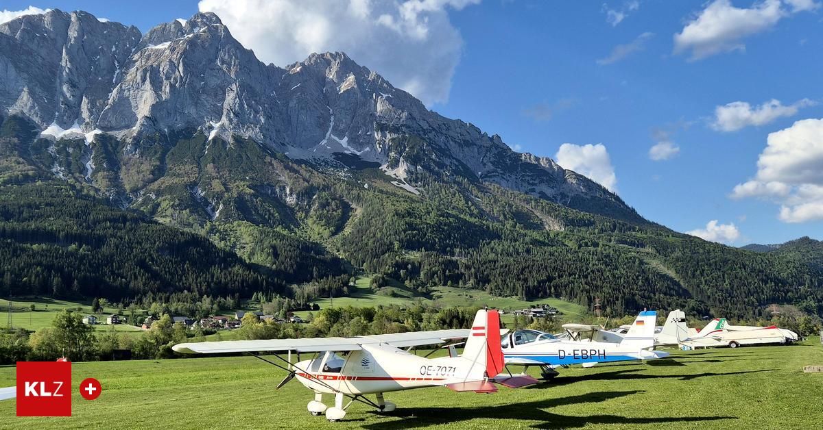 Mehrere kleine Flugzeuge sind auf einer Grasfläche mit Blick auf die Berge bei blauem Himmel geparkt.