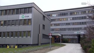 Ein Gebäude mit einem Schild mit der Aufschrift G G K an der Vorderseite, mehreren Fenstern und einem Weg davor.