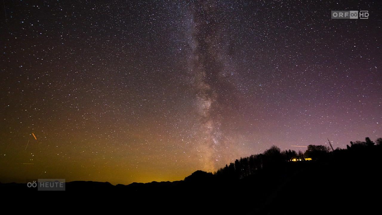 Der Nachthimmel ist voller Sterne und die Milchstraße ist sichtbar und taucht die Silhouette von Bäumen und Bergen in ein sanftes Licht.