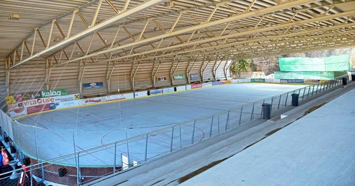 Eine leere Eishalle für Eishockey mit Metallgeländern und einem Mülleimer. Die Eisfläche hat blaue Markierungen und ist von Metallkonstruktionen umgeben.