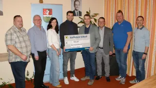 Eine Gruppe von Menschen posiert für ein Foto mit einem großen Scheck von Gemeinderat Hofkirchen in der Hand. Sie alle lächeln und scheinen sich in einem formellen Umfeld zu befinden.