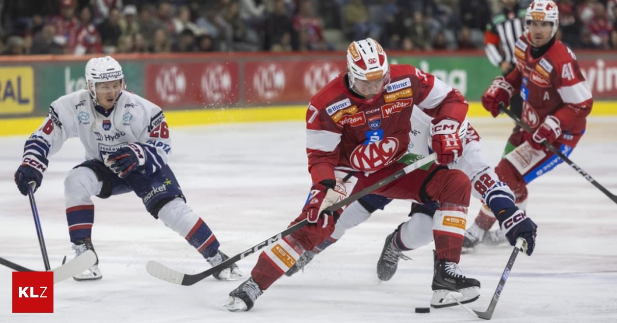 Eishockeyspieler in roten Trikots mit KAC auf ihren Jerseys spielen auf einer Eisbahn. Sie versuchen, den Puck zu bekommen.