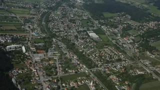 Luftaufnahme einer Stadt mit vielen Gebäuden, Straßen und Grünflächen. Die Stadt ist von Bäumen und Vegetation umgeben, durch die ein Fluss fließt.
