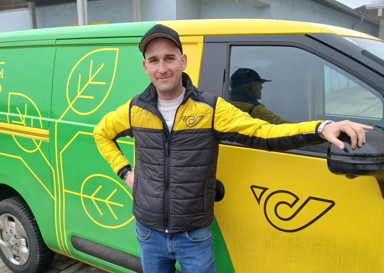 Ein Mann in einer gelb-schwarzen Jacke steht neben einem gelb-grünen Lieferwagen mit einem Blattdesign an der Seite.