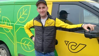 Ein Mann in einer gelb-schwarzen Jacke steht neben einem gelb-grünen Lieferwagen mit einem Blattdesign an der Seite.