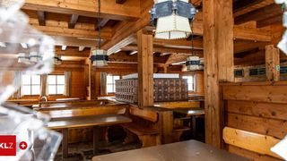 Ein leeres Holzrestaurant mit mehreren Tischen und Bänken sowie Holzbalken und hängenden Lampen.