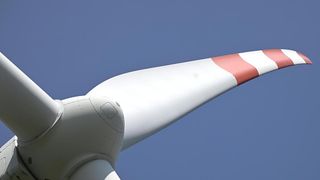 Ein Nahaufnahme einer Windturbinen-Flügelspitze gegen einen klaren blauen Himmel, die ihre weiße und rote Gestaltung zeigt.