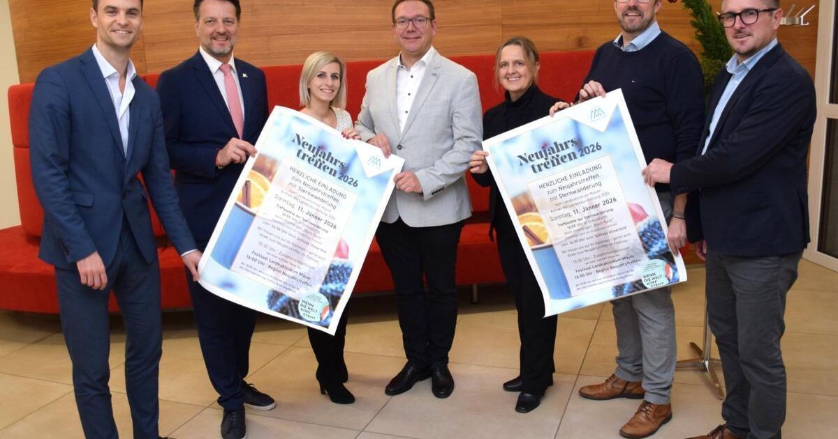 Fünf Personen in formeller Kleidung halten ein Plakat und posieren für ein Foto. Die Plakate tragen den Text 'Neujahrs treffen 2026' und ein Datum darauf. Der Hintergrund ist unscharf.
