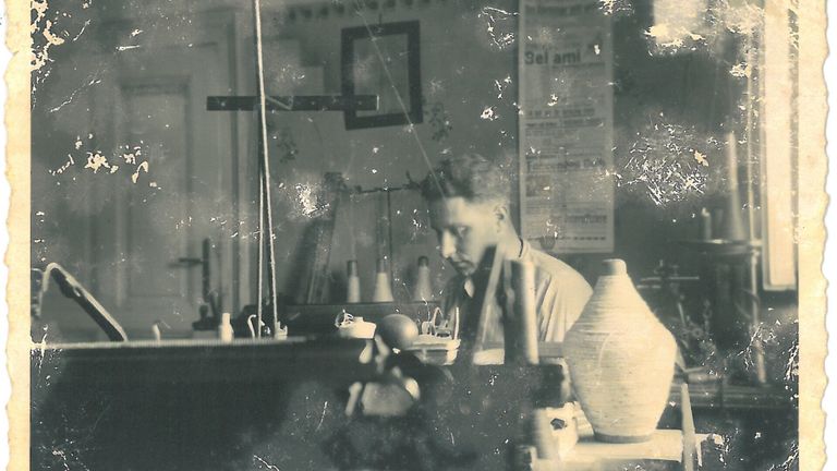 Ein Schwarz-Weiß-Foto einer Frau in einer Werkstatt, konzentriert auf ein Töpferprojekt. Sie sitzt mit Werkzeugen und Töpferstücken um sie herum.