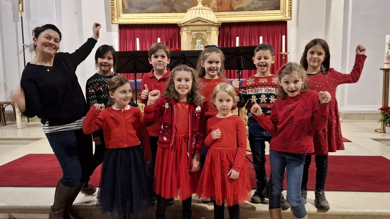 Eine Gruppe von Kindern in roten Kleidern posiert für ein Foto in einer Kirche, mit einem goldenen Altar und roten Vorhängen im Hintergrund.
