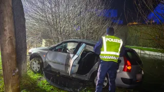 Ein Polizist in einer Warnweste steht neben einem beschädigten Auto am Straßenrand in der Nacht.