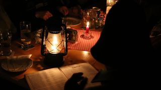 Ein schwach beleuchteter Tisch für eine Mahlzeit mit einer Laterne und einer Kerze, während jemand ein Buch mit dem Titel D. Moitsch liest.