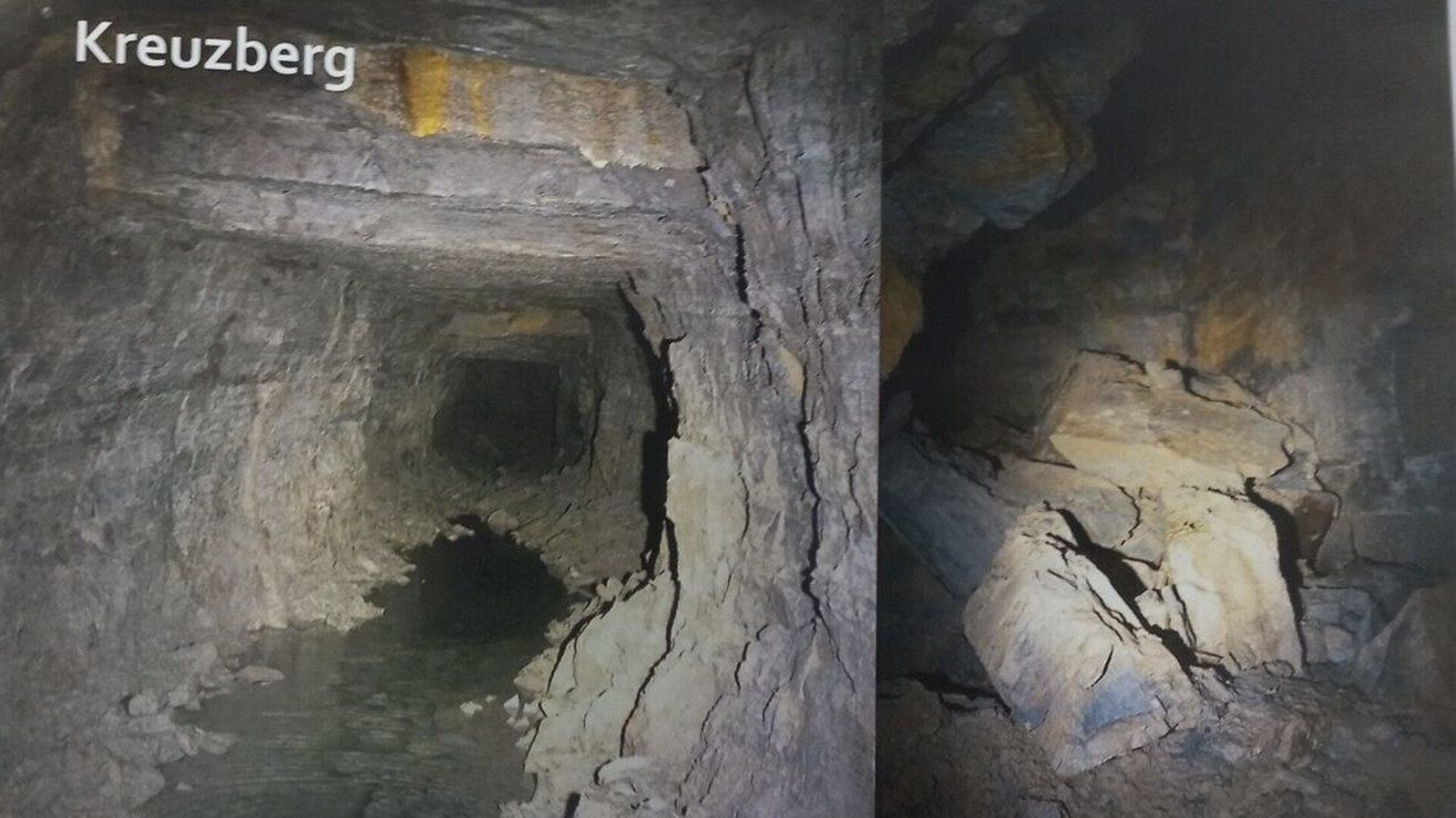 Das Bild zeigt einen Tunnel mit einem Wasserstrom, der hindurchfließt. Es sind Risse in den Wänden und Steine an den Seiten zu sehen. Der Tunnel scheint alt und abgenutzt zu sein.