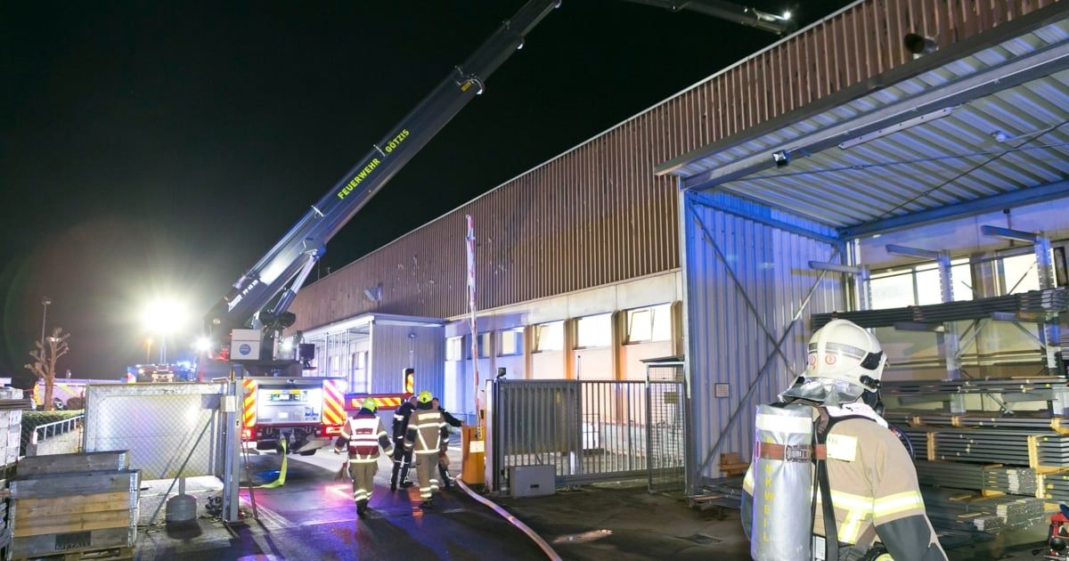 Feuerwehrleute reagieren auf einen Vorfall in einem Lagergebäude bei Nacht, mit einem Kran in der Nähe und mehreren Personen in Schutzausrüstung.