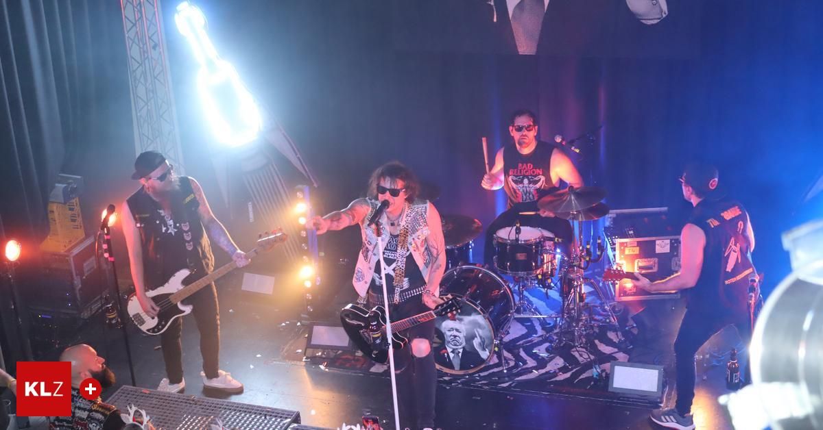 Eine Band spielt auf einer Bühne mit blauem Hintergrund. Der Leadsänger spielt Gitarre und singt in ein Mikrofon. Ein anderes Bandmitglied spielt Schlagzeug.