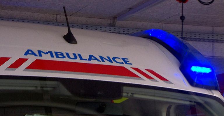 Nahaufnahme eines Krankenwagens mit dem Wort 'AMBULANCE' und roten und weißen Streifen. Die Notfallleuchte ist eingeschaltet.