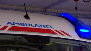 Nahaufnahme eines Krankenwagens mit dem Wort 'AMBULANCE' und roten und weißen Streifen. Die Notfallleuchte ist eingeschaltet.