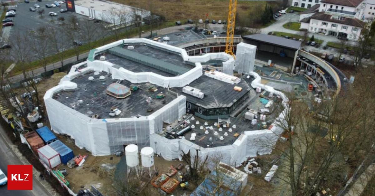 Eine Draufsicht auf eine Baustelle mit einem im Bau befindlichen Gebäude. Das Gebäude ist mit weißen Plastikplanen bedeckt. In der Nähe steht ein Kran und mehrere geparkte Fahrzeuge.