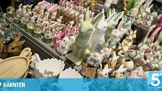 Eine Ausstellung zahlreicher Osterhasen in verschiedenen Farben und Größen, einige halten Eier und Blumen, angeordnet auf Regalen mit einem Schild mit der Aufschrift 'Karnten' im Vordergrund.