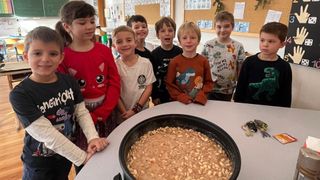 Eine Gruppe von Kindern im Klassenzimmer, die lächelnd für ein Foto posieren, mit einer Schüssel mit Nüssen im Vordergrund.