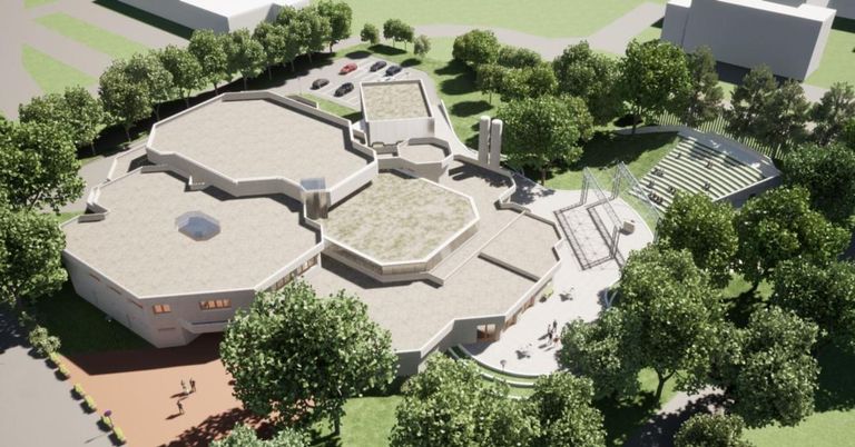 Ein Blick von oben auf ein modernes Gebäude mit sechseckigen Formen, umgeben von grünem Gras und Bäumen. Mehrere Autos sind auf dem Parkplatz geparkt. Menschen gehen herum.