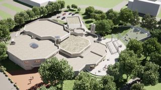 Ein Blick von oben auf ein modernes Gebäude mit sechseckigen Formen, umgeben von grünem Gras und Bäumen. Mehrere Autos sind auf dem Parkplatz geparkt. Menschen gehen herum.