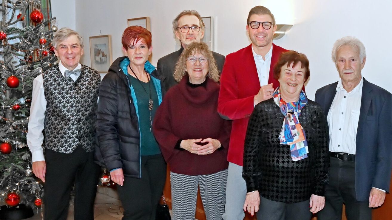 Eine Gruppe von Erwachsenen, drei Frauen und zwei Männer, stehen eng beieinander. Sie lächeln für ein Foto. Die Frau auf der linken Seite trägt eine schwarze Jacke. Die Frau in der Mitte trägt ein kastanienbraunes Rollkragenshirt. Der Mann auf der rechten Seite trägt eine rote Jacke.