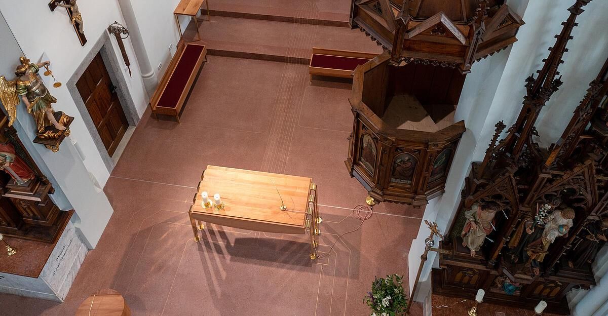 Eine Draufsicht auf das Innere einer Kirche mit einem hölzernen Altartisch, der zwei Kerzen hält. Eine Kanzel befindet sich auf der rechten Seite des Altars. Zwei Bänke sind auf der linken Seite, mit einer Lampe an der Wand befestigt.