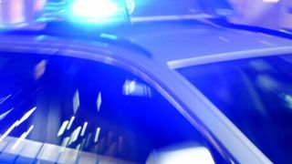 Ein Polizeiwagen mit blinkenden blauen Lichtern, der nachts auf einer Straße fährt.