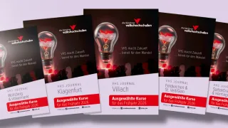 Drei VHS-Journal-Broschüren der Kärntner Volkshochschulen werden gezeigt. Jede Broschüre zeigt eine leuchtende Glühbirne und den Text 'VHS macht Zukunft...bereit für den Wandel.' Die Broschüren sind mit 'Klagenfurt', 'Villach' und 'Feldkirchen & St. Veit/Glan' betitelt. Sie heben ausgewählte Kurse für das Frühjahr 2026 hervor.