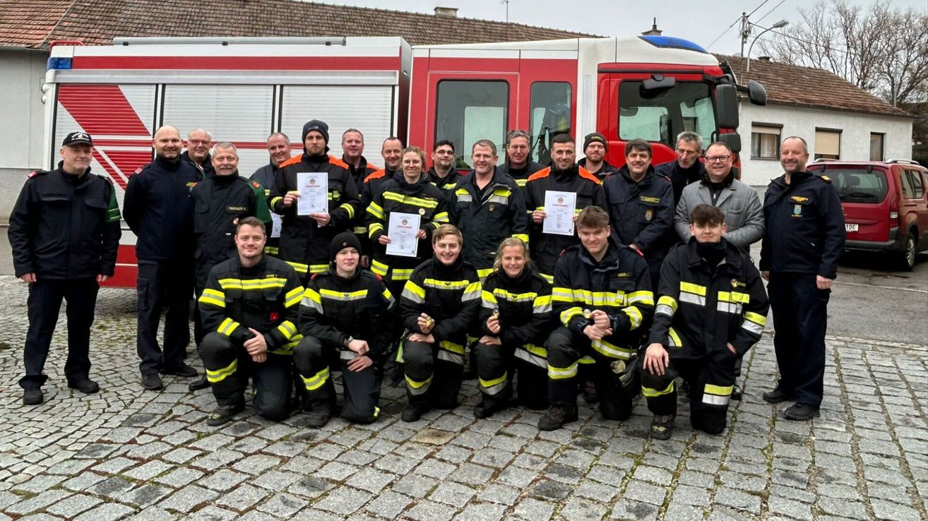 Eine Gruppe von Feuerwehrleuten in Uniformen posiert vor einem Feuerwehrauto und hält Urkunden in der Hand.