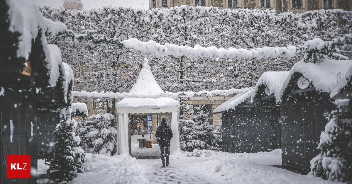 Eine Person in einem schwarzen Mantel geht durch einen verschneiten Bereich mit einem weißen Zelt, das mit Schnee bedeckt ist.