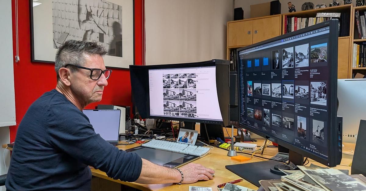 Ein Mann mit Brille arbeitet an einem Schreibtisch mit zwei Monitoren, einer zeigt eine Foto-Raster, in einem Büro.
