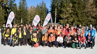 Eine Gruppe von Menschen mit Medaillen und Jacken, die in einem verschneiten Bereich für ein Foto posieren, mit Bäumen und einem Gebäude im Hintergrund.