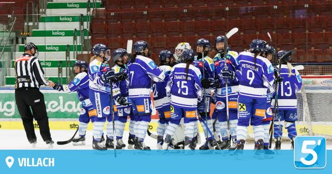 Eine Eishockeymannschaft in blauen Uniformen ist auf dem Eis versammelt. Ein Schiedsrichter steht in der Nähe, und der Hintergrund zeigt leere rote Tribünen.