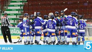 Eine Eishockeymannschaft in blauen Uniformen ist auf dem Eis versammelt. Ein Schiedsrichter steht in der Nähe, und der Hintergrund zeigt leere rote Tribünen.
