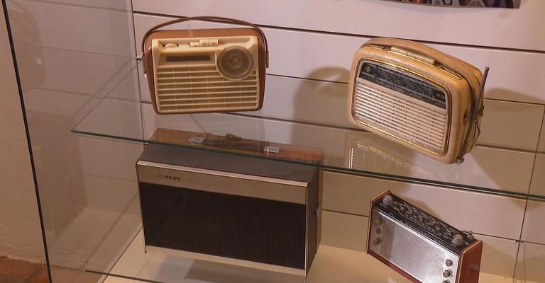 Vier Vintage-Radios sind auf einem Glasregal ausgestellt. Oben links hat ein großes Drehrad, oben rechts ist kleiner, unten links hat ein Philips-Etikett, und unten rechts ist ein kleineres Modell.
