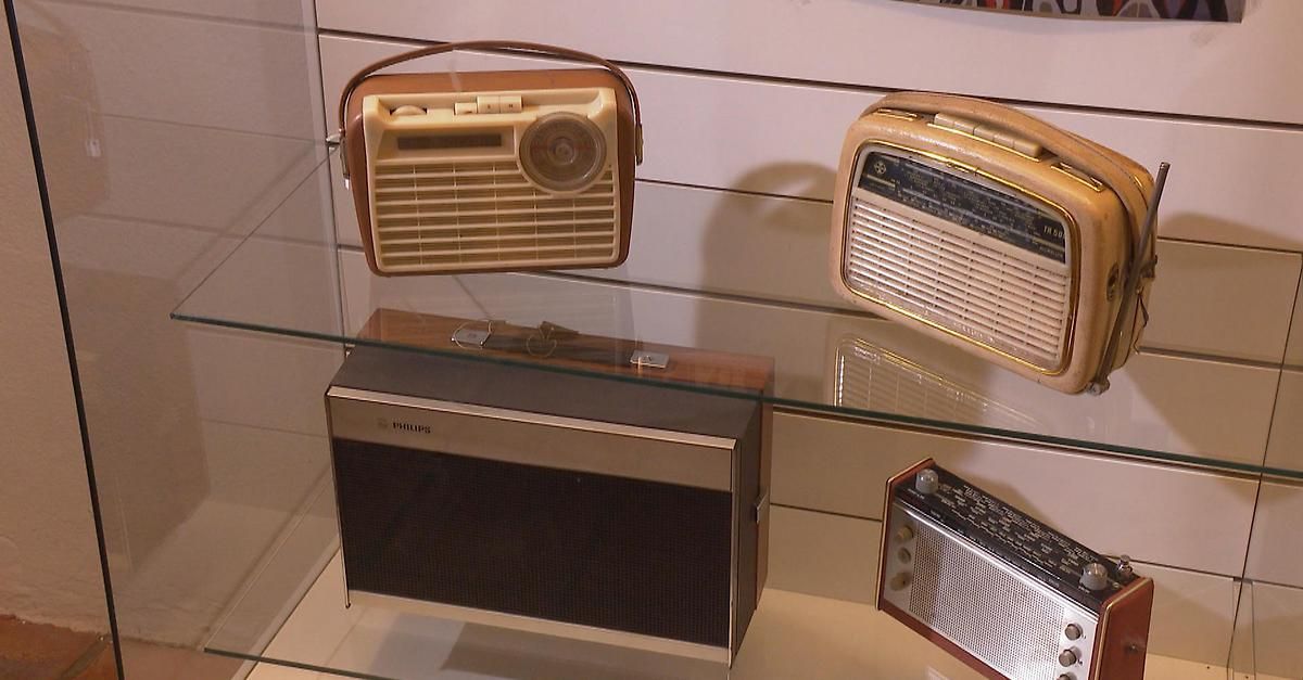 Vier Vintage-Radios sind auf einem Glasregal ausgestellt. Oben links hat ein großes Drehrad, oben rechts ist kleiner, unten links hat ein Philips-Etikett, und unten rechts ist ein kleineres Modell.