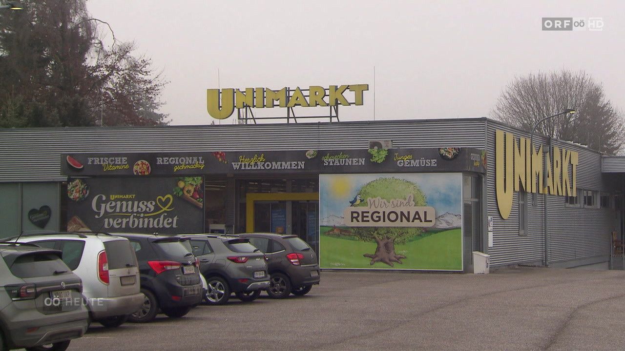Der Eingang zu einem Unimarkt-Geschäft mit einem Slogan, der 'Wir sind regional' lautet. Der Laden hat ein großes Schild mit dem Wort 'Regional'. Mehrere Autos sind davor geparkt.