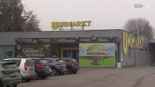 Der Eingang zu einem Unimarkt-Geschäft mit einem Slogan, der 'Wir sind regional' lautet. Der Laden hat ein großes Schild mit dem Wort 'Regional'. Mehrere Autos sind davor geparkt.