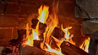 Ein Backsteinkamin mit einem brennenden Feuer, umgeben von Holzscheiten, Steinen und einem hölzernen Kaminsims, strahlt eine warme Glut aus.
